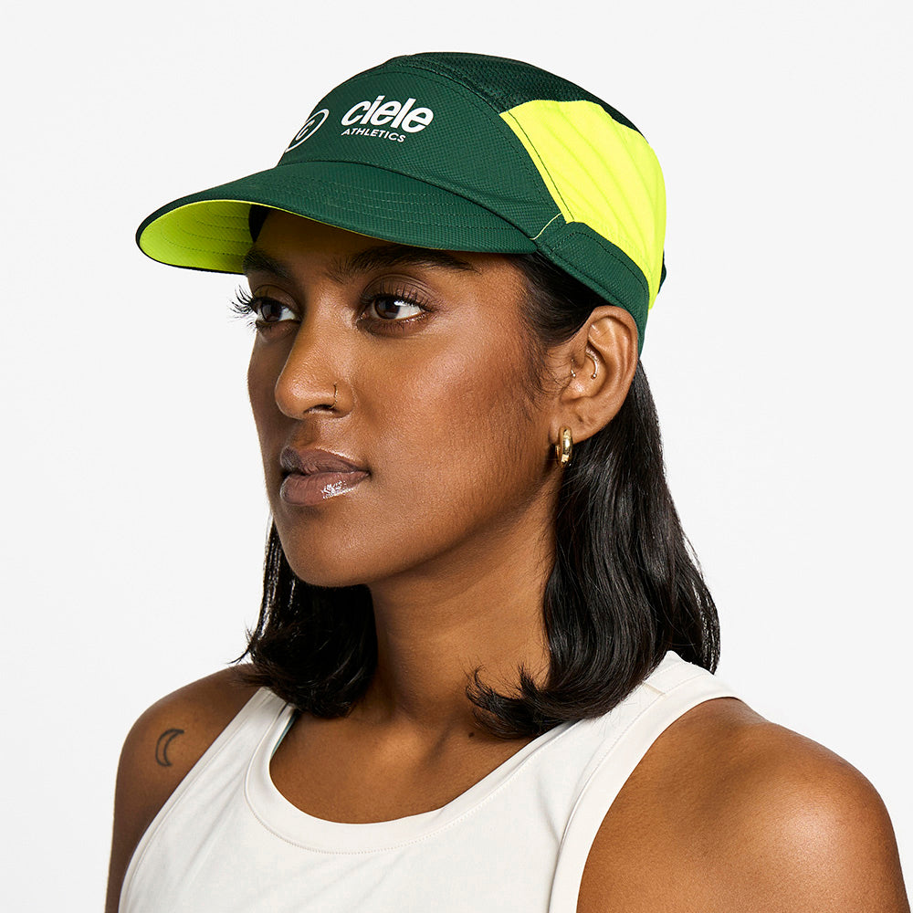 side view of the ciele athletics FTSCap unisex running hat with a curved brim in emerald color, on a model