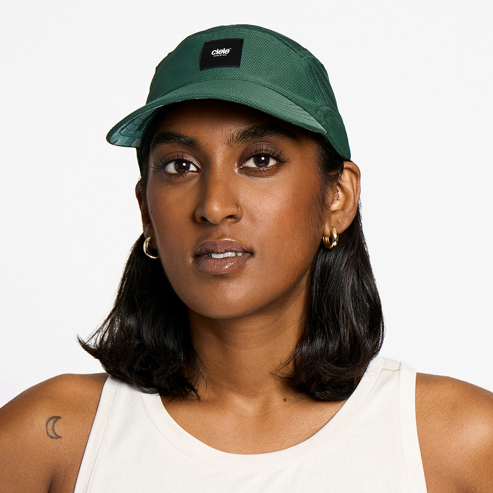 side view of the ciele athletics FTSCap unisex running hat with a curved brim in emerald color, on a model